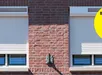 Roodbruine rolschuifraam met witte kozijnen in een bakstenen gevel