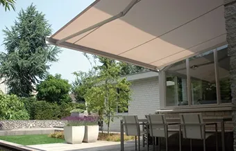 Zonwering in beige gekoppeld aan buitenmuur met buitenkeuken en tuinmeubilair
