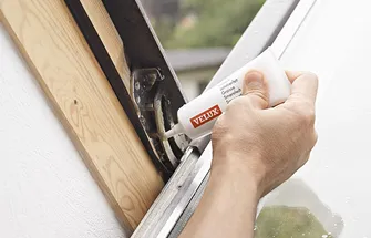 Hand met tube Velux reinigingsmiddel aangebracht op dakraamframe