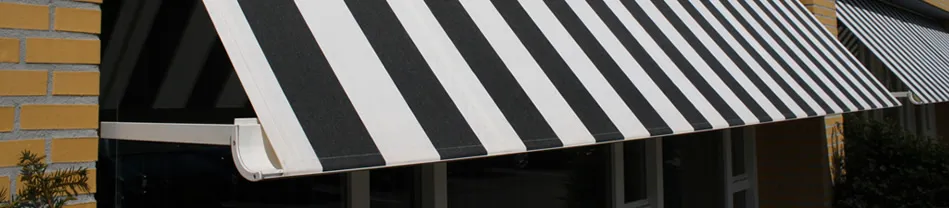 Zwart-witte gestreepte buitenzonwering onder een dakrand van een huis