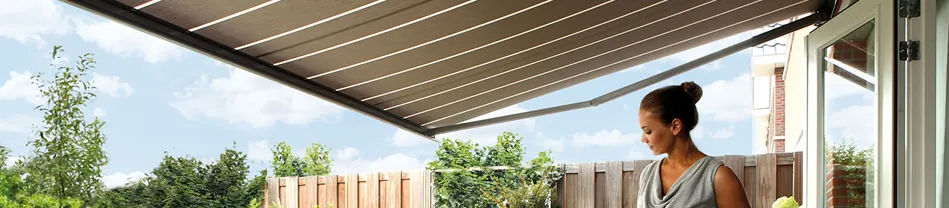 Vrouw staat onder een beige buitenzonwering aan de buitenzijde van een huis met tuin