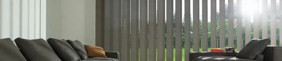 Grijze lamellen zonwering voor groot raam in woonkamer met donkere banken en tafel