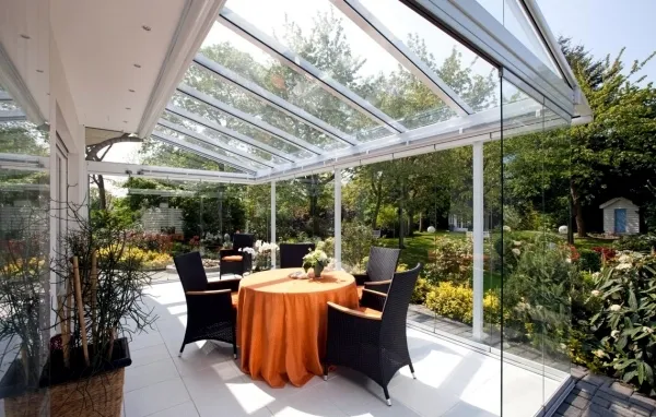 Glas terrasoverkapping met tafel en stoelen in tuin met groen en bloemen