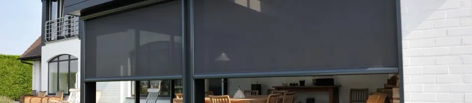 Grijze buitenzonwering gespannen voor grote schuifdeuren van een woonhuis met terrasmeubilair