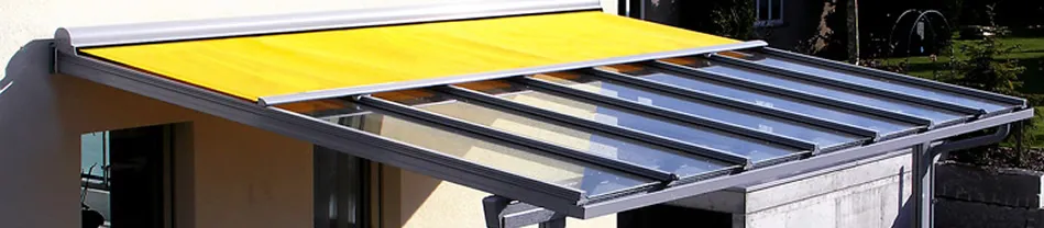 Geel zonnescherm gemonteerd boven een glazen verandadeur met metalen frame